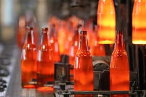 Production line of glass bottle glowing after coming out of the oven that uses abrasion anchors to hold refractory lining in oven.
