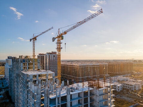 Cranes on the construction site using structural devices known as castable anchors surrounded by new real estates. Scenic aerial photo of growing city districts.