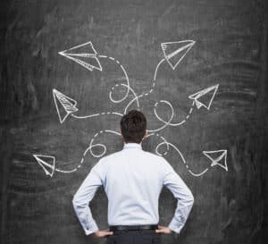 Rear view of a man in formal clothes who is pondering about possible solutions of the complicated problem. Many arrows with different directions are drawn around his head on the black chalkboard. Refractory Anchor Types - Refractory Anchors Inc
